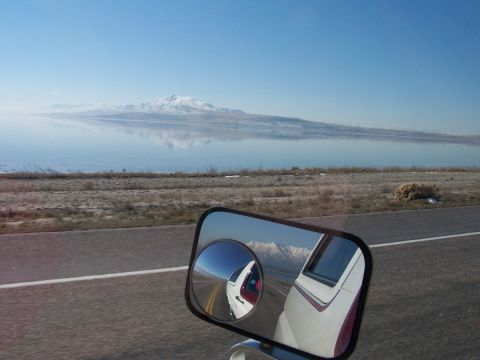 1990 Ford Bronco - Reflection in the side mirror shows a white vehicle with red trim driving on a road with mountains in the background.