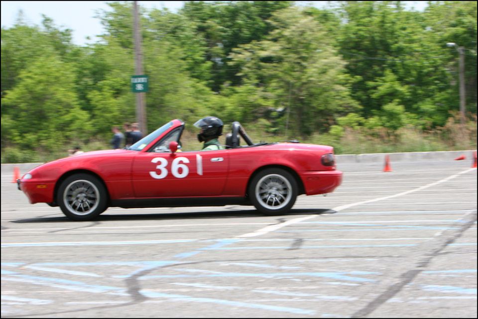 Red convertible sports car, number 361 on door, driving on a track with orange cones