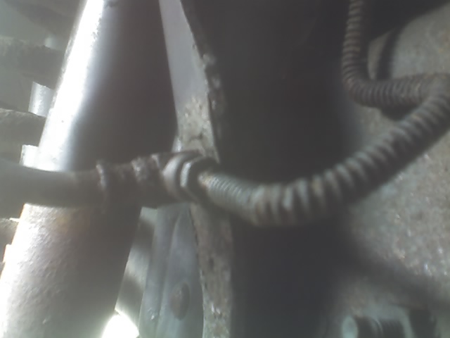 Close-up of a rusty brake line connected to a suspension component, with a corrugated hose visible