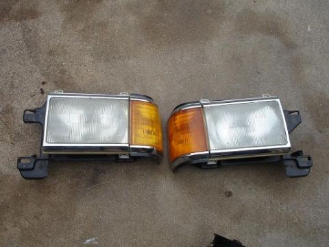 1996 Ford F-150 - Two headlights with chrome trim and amber turn signal sections are displayed side-by-side on a concrete surface.