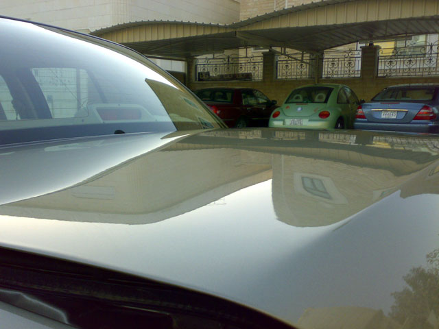 Silver car hood reflecting a building and other cars parked under a carport