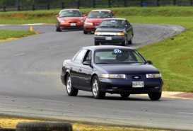 1997 Ford Taurus - A dark blue Ford Taurus navigates a turn on a race track, with other vehicles following closely behind.