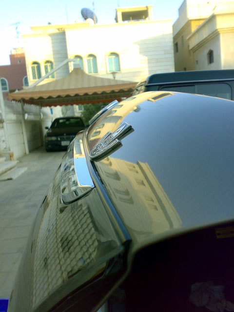 2007 Mercury Grand Marquis - Close-up of a dark metallic car trunk chrome trim and an emblem, with another vehicle visible in the background.
