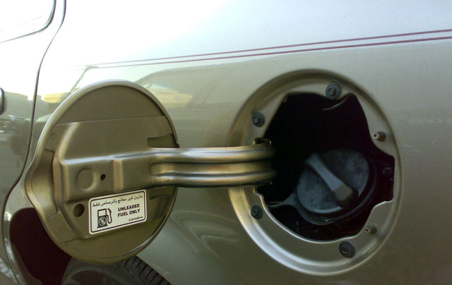 Close-up of a car's fuel door open, showing the gas cap inside. Sticker says 'UNLEADED FUEL ONLY'