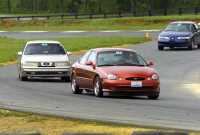 1997 Ford Taurus - Three sedans race on a paved track with green trees and grass in the background.
