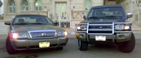 2007 Mercury Grand Marquis - A Mercury Grand Marquis and an SUV are parked side-by-side in front of a building with arched windows.