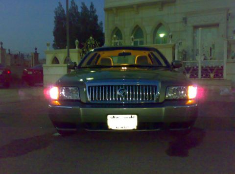 2007 Mercury Grand Marquis - The front of a Mercury Grand Marquis is visible with its headlights illuminated, parked in front of a building.