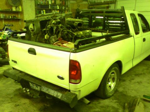 1982 Ford Bronco - A white pickup truck is loaded with engine components in its bed, viewed from the rear.