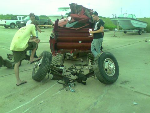 1982 Ford Bronco - People examine a heavily damaged truck chassis outdoors, with other vehicles and a boat in the background.