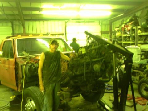 1982 Ford Bronco - A man stands next to an orange truck in a garage, with its engine removed and an engine hoist nearby.