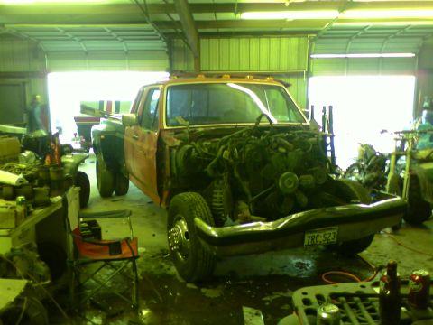 1982 Ford Bronco - Truck in garage with engine removed, showing empty engine bay and dually rear wheels.