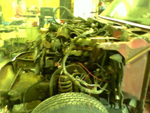 1982 Ford Bronco - The engine bay of a vehicle is shown with a complex arrangement of wires and hoses, with a tire in the foreground.