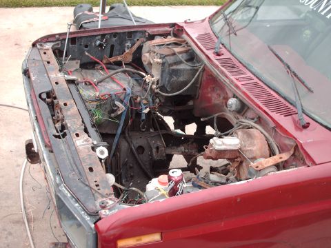 1982 Ford Bronco - The engine bay of a red vehicle, possibly from the early 1980s, shows significant disarray and rust.