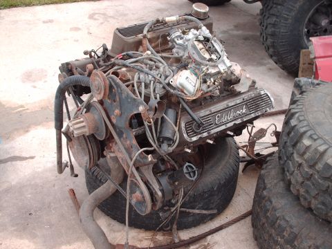 1982 Ford Bronco - Engine assembly with Edelbrock valve covers sits on tires, with other vehicle parts nearby.
