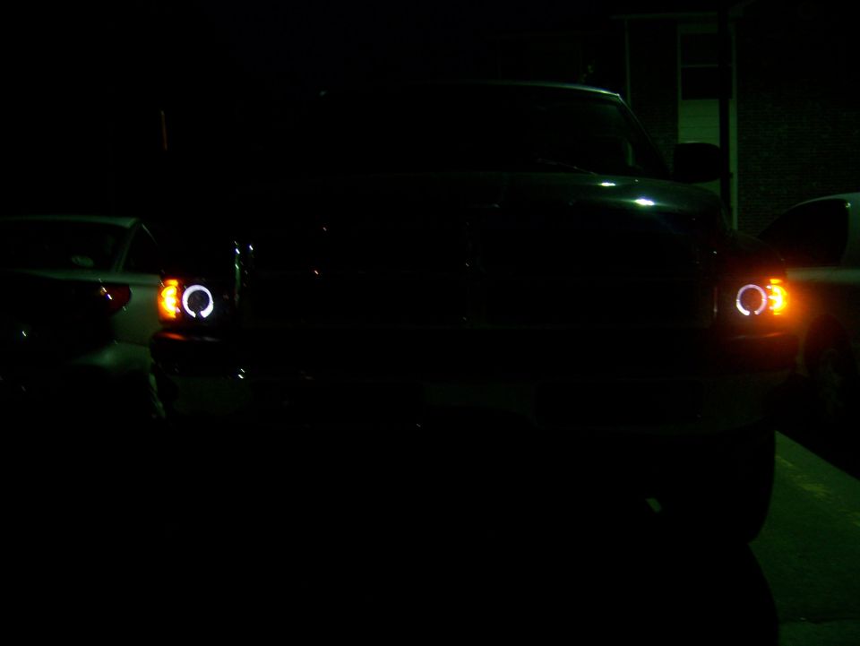 Front view of a 2001 Dodge 1500 with halo headlights on at night. Another vehicle is partially visible to the left