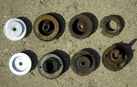 1997 Ford Taurus - A collection of old and new vehicle suspension parts are displayed on a rough, outdoor surface.