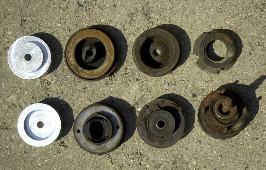 Several used and one new suspension component, possibly strut mounts, laid out on a concrete surface