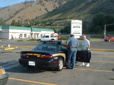 2000 Ford Crown Victoria - A dark blue police car is parked in a lot with a white pickup truck in the background. Two men are standing by the police car.