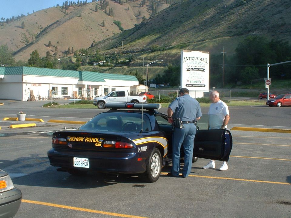 Dark blue police car with "HIGHWAY PATROL" text on rear, parked next to a white pickup truck