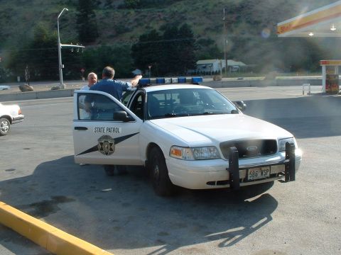 2000 Ford Crown Victoria - A white Ford Crown Victoria police car is parked at a gas station with the driver's door open.