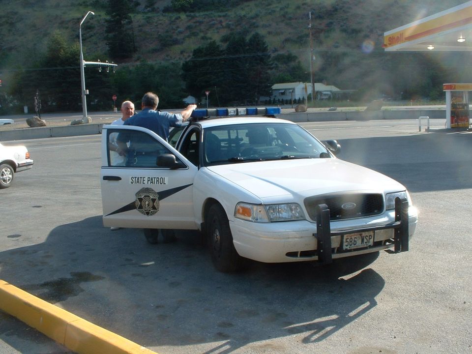 White Ford Crown Victoria police car with open driver's door, "STATE PATROL" text, and push bumper