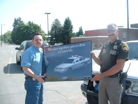 2000 Ford Crown Victoria - Two men hold a poster a police car and the slogan 'Not every superhero gets to drive a Crown Vic.'
