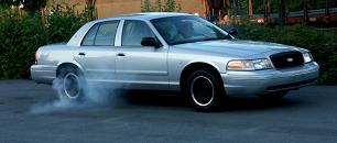 1998 Ford Crown Victoria - A silver sedan is performing a burnout, creating a cloud of smoke from its rear tires.
