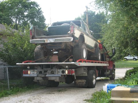1978 Ford Bronco - A lifted pickup truck is loaded onto a flatbed tow truck, with a white car visible in the background.