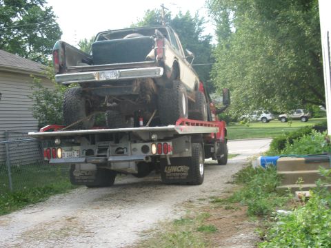 1978 Ford Bronco - A lifted 1978 Ford Bronco is transported on a flatbed tow truck, with other vehicles visible in the background.