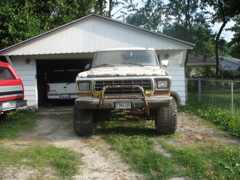 1978 Ford Bronco - This weathered pickup truck is parked in front of a garage, with two other vehicles partially visible.