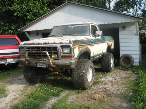 1978 Ford Bronco - A weathered Ford F-Series truck sits outside a garage, showing signs of age and modification.