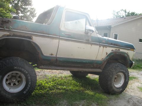 1978 Ford Bronco - Side view of a weathered 1978 Ford Bronco with two-tone paint and extensive rust.