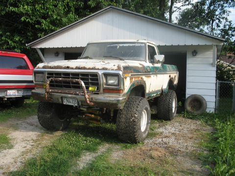 1978 Ford Bronco - A heavily modified, older model Ford pickup truck sits in front of a garage.