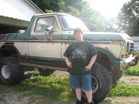 1978 Ford Bronco - A boy poses with a lifted 1978 Ford Bronco, showing off its off-road tires and two-tone paint.