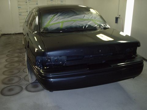 1996 Ford Crown Victoria - A dark sedan is in a paint booth, ready for refinishing. The rear bumper and taillights are removed.