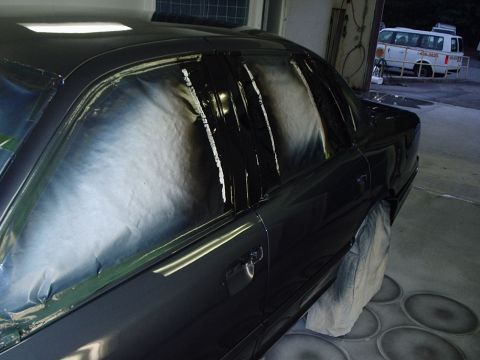 1996 Ford Crown Victoria - A dark-colored sedan is being prepped for refinishing, with its windows covered in tape.
