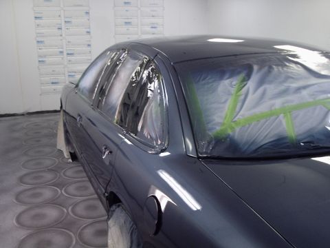 1996 Ford Crown Victoria - A car is being prepped for painting inside a booth, with windows covered in plastic and tape.