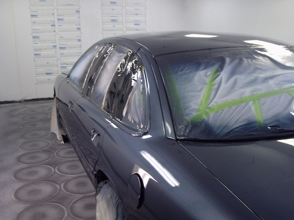 Dark sedan with windows taped off, sitting in a paint booth