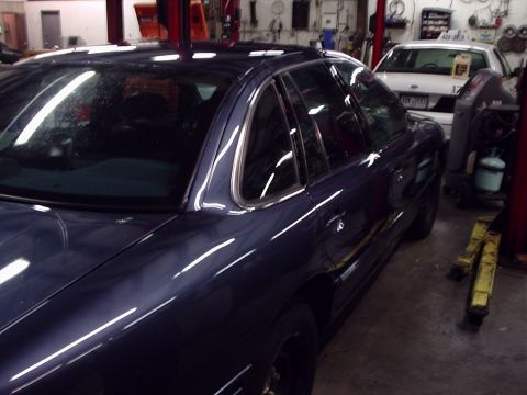 1996 Ford Crown Victoria - A dark blue sedan is parked in a garage, with another white vehicle visible in the background.