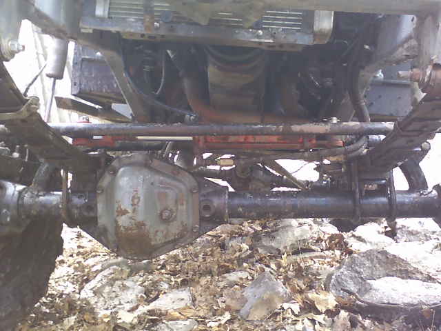 Undercarriage of a heavily modified off-road vehicle, showing a large differential, leaf springs, and engine components
