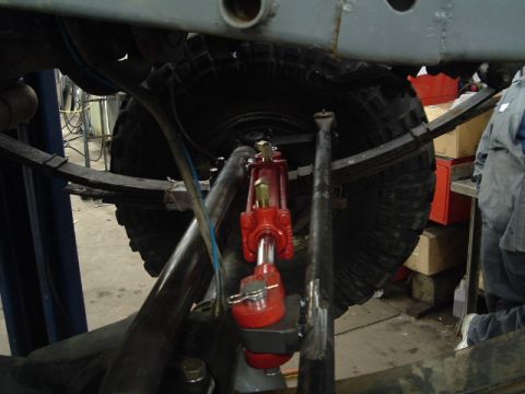 1991 Ford Bronco - Close-up view of a red hydraulic cylinder installed on a vehicle's suspension system, near a large tire.