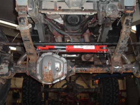 1991 Ford Bronco - Undercarriage of a vehicle, focusing on the suspension and a newly installed red steering stabilizer.