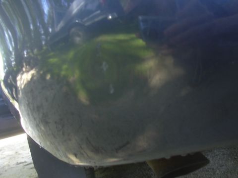 1996 Ford Crown Victoria - Reflection of a dark sedan on a dirty car bumper shows trees and sky.