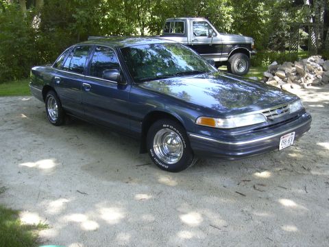 1996 Ford Crown Victoria - A dark blue 1996 Ford Crown Victoria is parked on a gravel surface, with a pickup truck visible in the background.