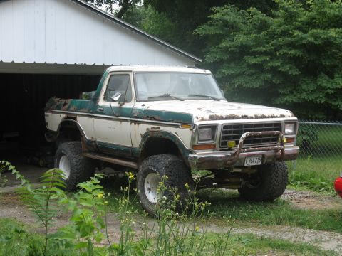 1978 Ford Bronco - A lifted 1978 Ford Bronco sits parked in front of a garage, showing signs of wear and tear.