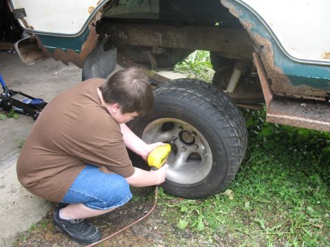 1978 Ford Bronco - A person works on a vehicle's wheel, revealing significant rust on the body and frame.