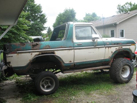 1978 Ford Bronco - A heavily rusted, two-tone white and teal Ford Bronco sits outdoors, lifted on large tires.