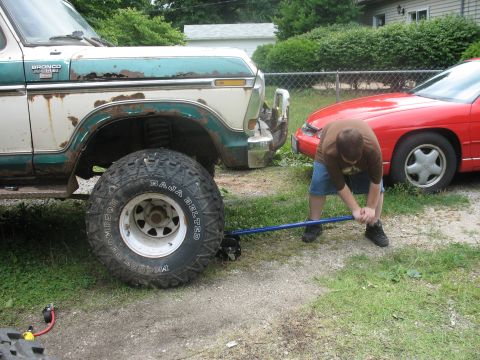 1978 Ford Bronco - Man jacks up a rusty 1978 Ford Bronco next to a red car in a driveway.
