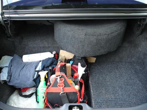 1999 Ford Crown Victoria - Open trunk of a dark sedan with gray carpeted floor and a carpet-covered spare tire hump along the back wall. The left side is loaded with…