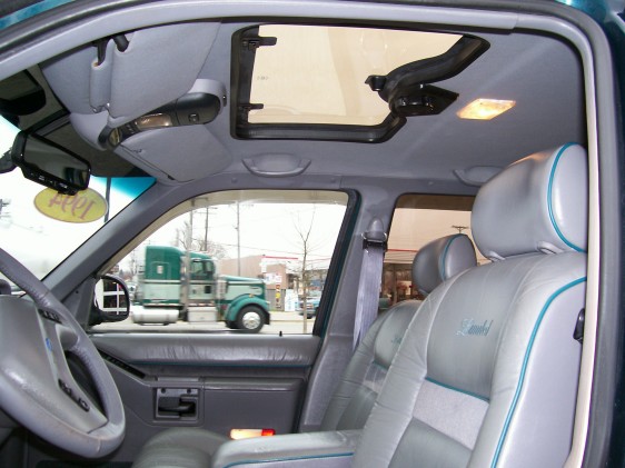 Interior shot of a 1994 Ford Explorer showing gray leather seats with teal trim, a sunroof, and two trucks visible through the window